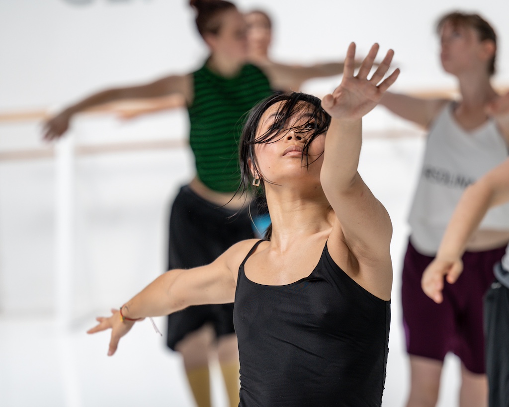 A dancer extends her arms during a training session in a dance studio